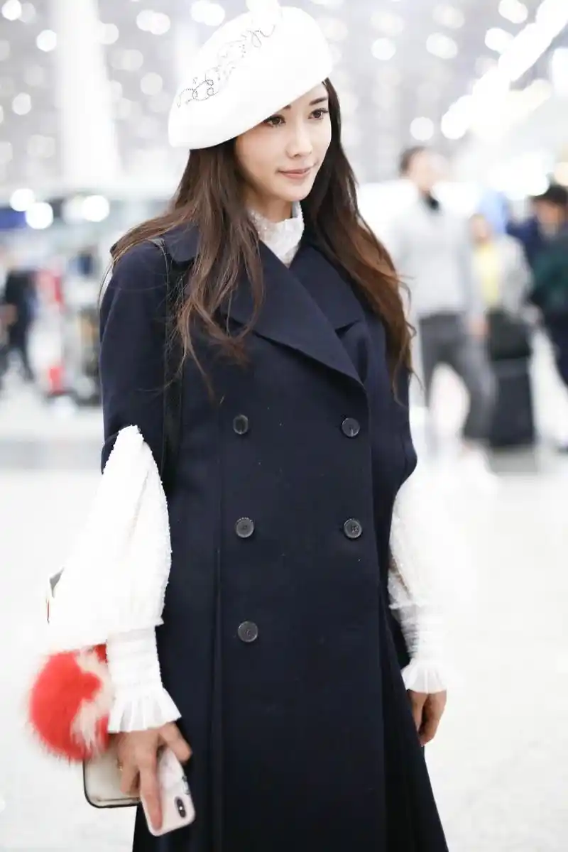 林志玲戴白色贝雷帽穿黑色长款大衣现身机场,皮肤白皙面带微笑