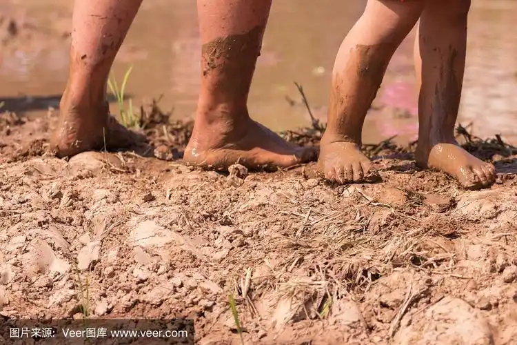 光着脚在泥里,男孩的腿在泥泞的水坑里玩耍后