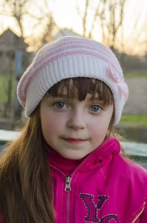 小女孩,在蓝色的大眼睛看着相机草背景上的白帽子的粉红色上衣的小