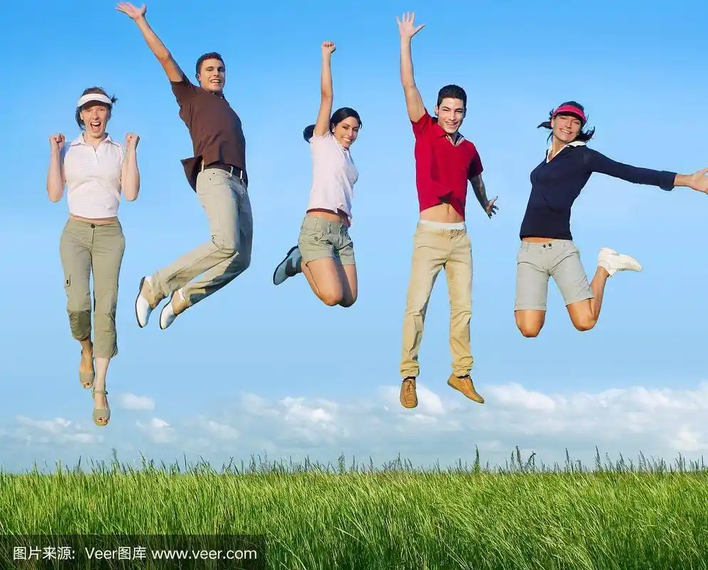 跳跃的年轻人在草地上快乐的团体