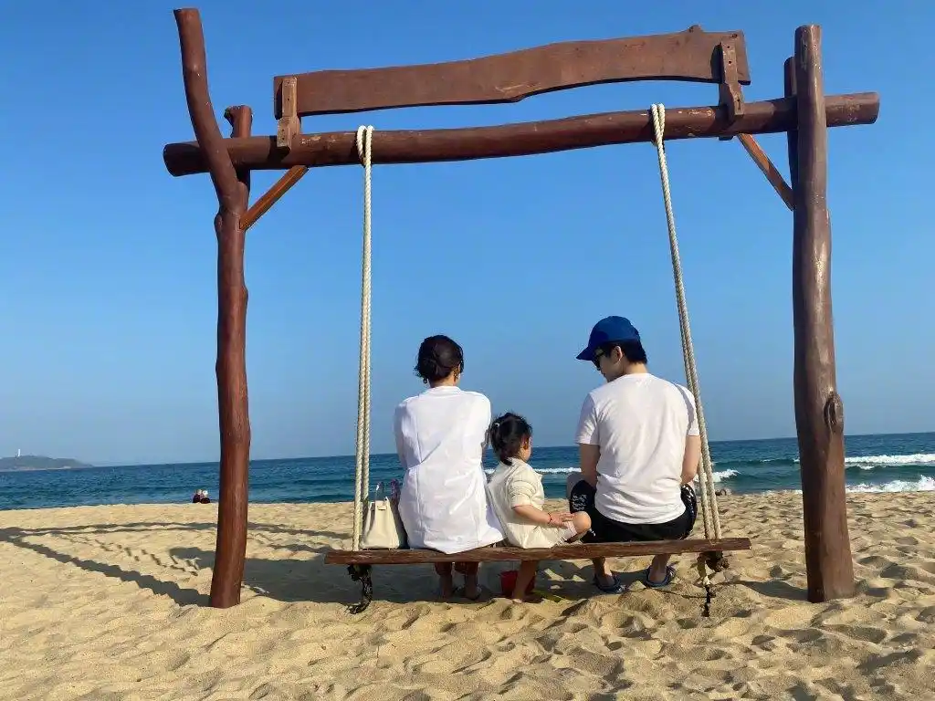 一家三口面朝大海坐在秋千上,虽然看不到他们的正脸,但是背影杀也是