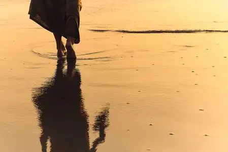 浪漫的少女赤脚在沙滩上漫步.日落时,女人光着脚在海里散步.