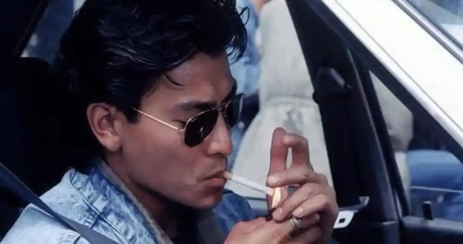 刘德华穿着一件黑色的皮肤,站在街边抽烟,刘德华抽烟的动作很简单