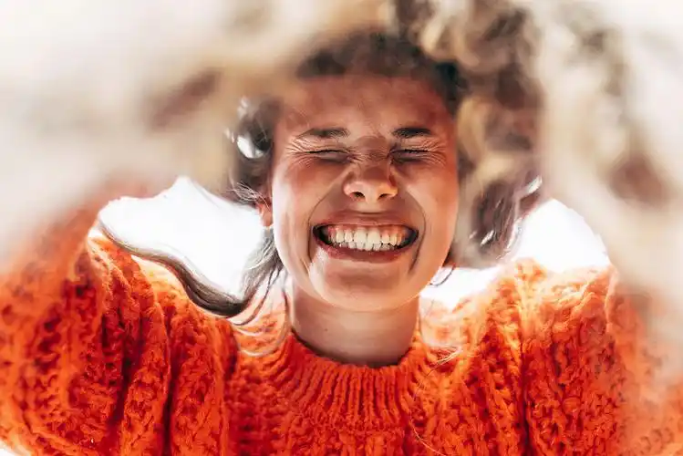 的牙齿,身穿橙色毛衣,脸上洋溢着快乐的表情,在天空的背景上摆姿势