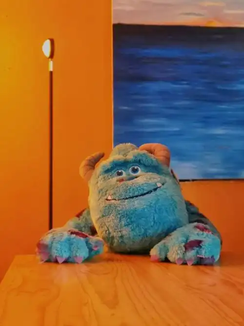 室内暖光下怪兽大学的蓝毛怪萨利文静静地坐在桌前望着你