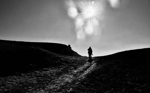 逆光中,一个背影沿着崎岖的山路向远方走去.