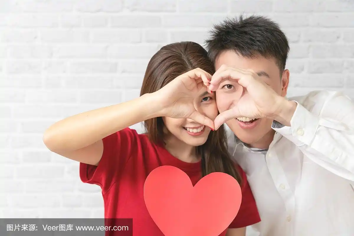 一对年轻夫妇正在做心形手势,微笑着看着镜头.情人节的概念.
