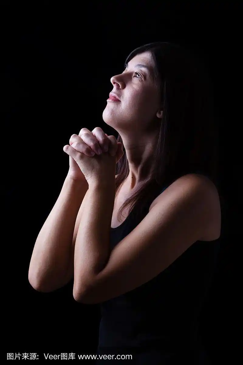 虔诚的女子在黑色背景上,双手合十,满怀希望地仰望上帝,虔诚地向上帝