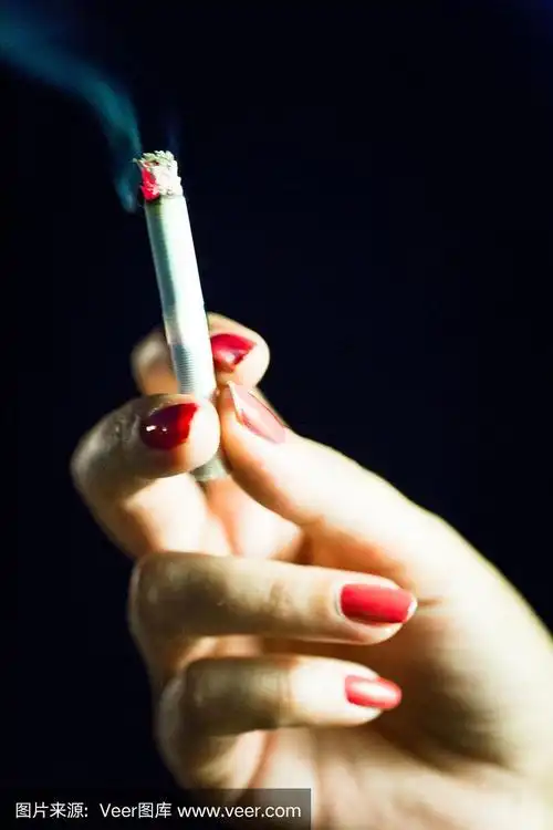 涂着红色指甲油的女性手拿着点燃的香烟