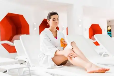 一位美女手拿瓶子,用身体油涂在腿上照片