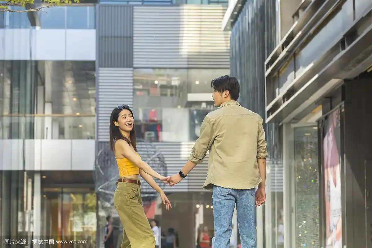 青年情侣在户外商业街手牵手浪漫逛街旅行