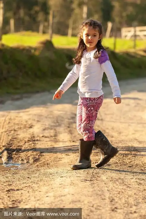 小女孩穿着雨靴在泥地里玩耍