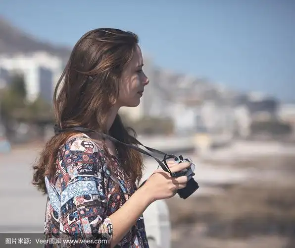 美丽的年轻女子拿着相机,侧面,在海边