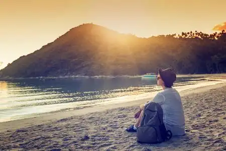 敬佩年轻女人旅行者坐在阳光下的海滩上.她敬佩 t照片