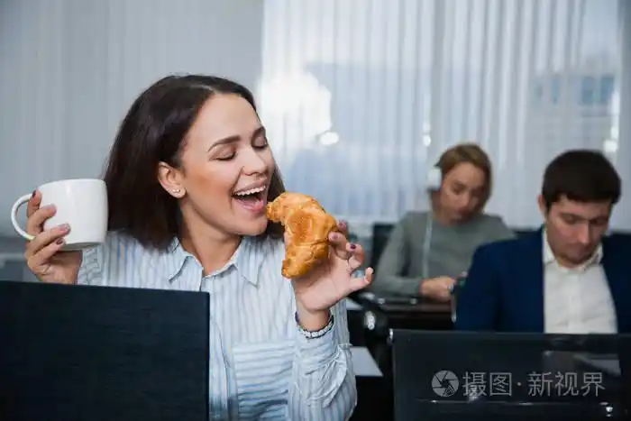 放松的女学生与杯茶或咖啡和小吃牛角面包和苹果一群人在背景上快乐的