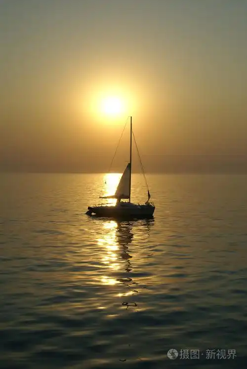 在日落时在平静的海面上航行的小帆船游艇