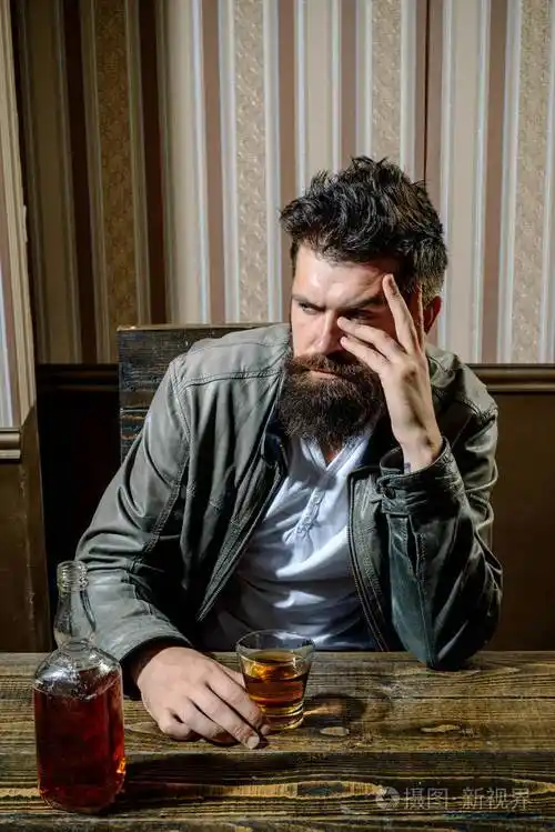 拿着一杯威士忌的人.英俊时髦的胡子男人下班后在家喝酒.