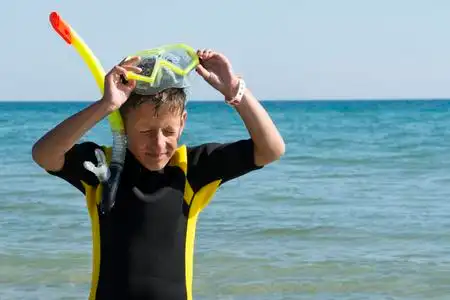 穿潜水衣的男孩脱下面具, 在海里浮潜照片
