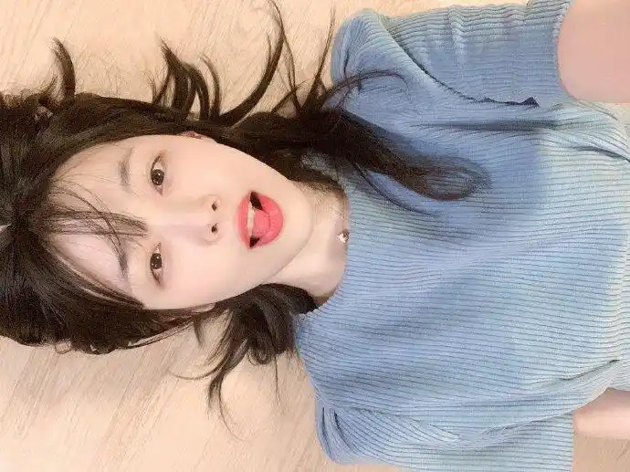 照片中雪莉身穿蓝色上衣,躺在地板上,单手举起手机自拍,张着嘴巴搞怪